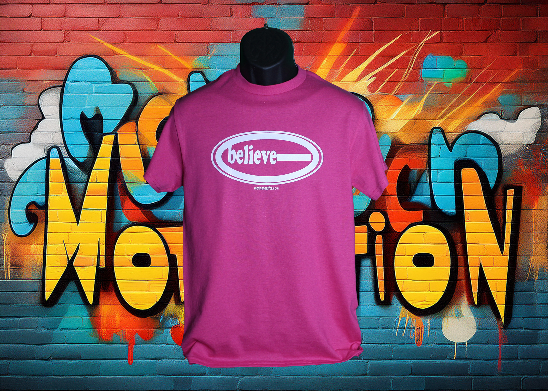 Pink T Shirt with the word Believe written on the front in White ink. With the words motivategifts.com written below image centered